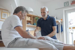 alt="Kinésithérapeute en polo utilisant la Tecarthérapie sur un patient âgé atteint de pathologies chroniques dans un cabinet moderne"